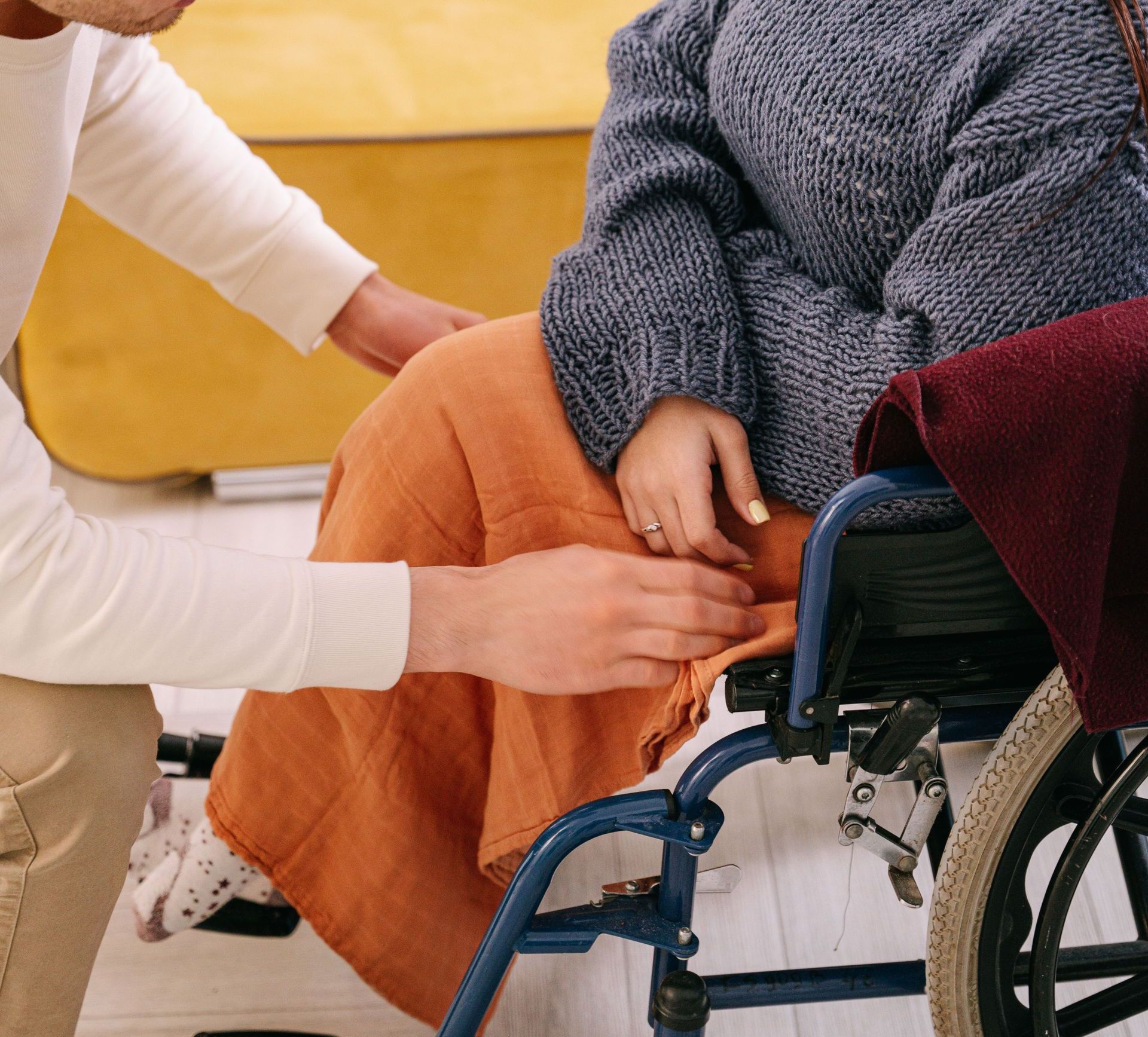 A supportive man assisting a woman in a wheelchair indoors, reflecting care and companionship.