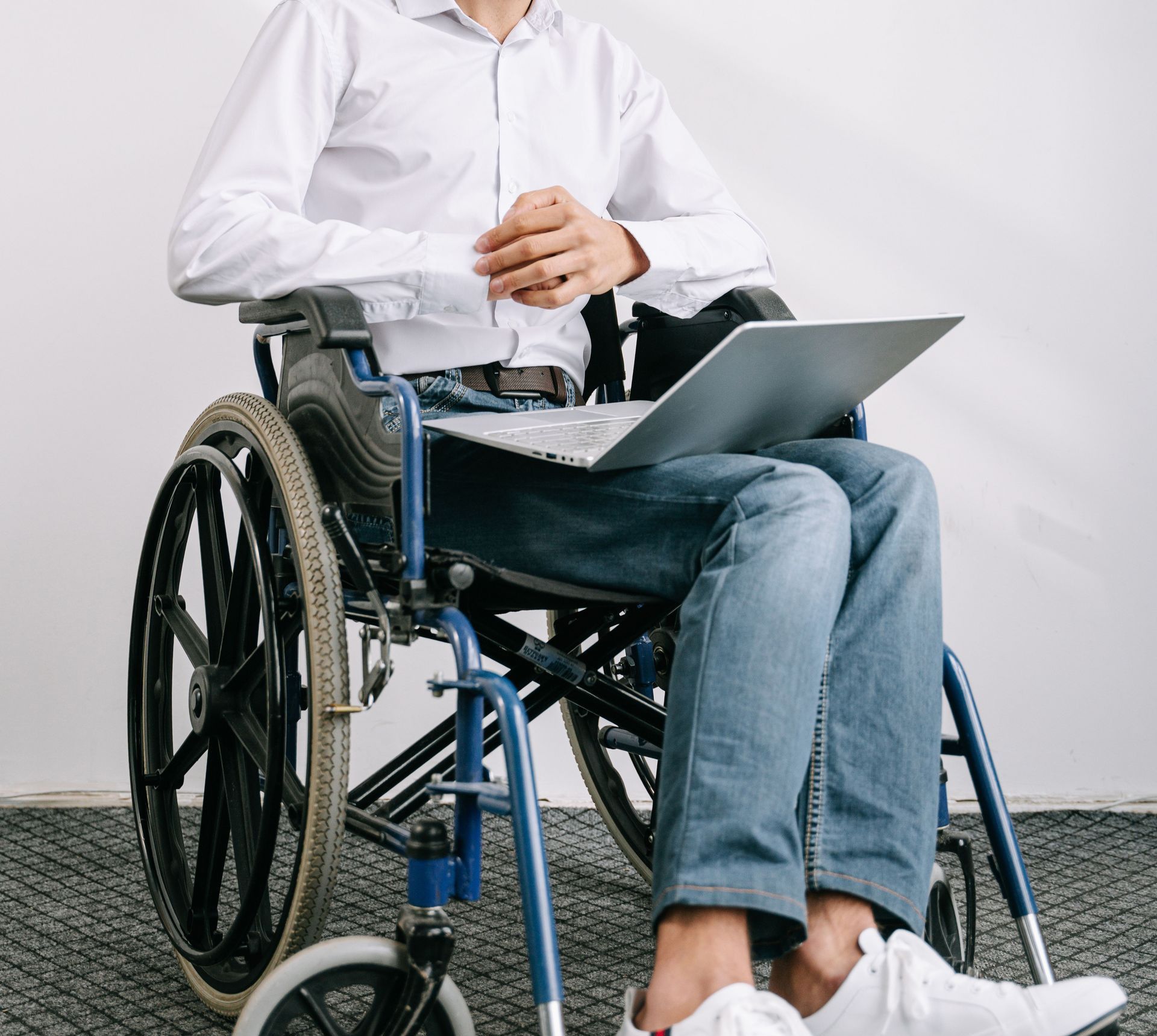 Confident bearded man in wheelchair using laptop while smiling in a bright office setting.